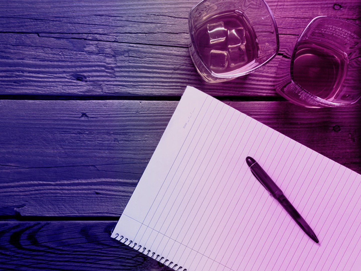 Ein offener Notizblock mit einem schwarzen Stift und zwei Gläsern Wasser auf einem Holztisch.