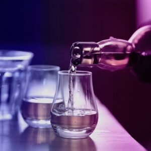 Eine Flasche Whisky wird in ein Glas gegossen, während zwei weitere Gläser auf einem Tisch stehen.