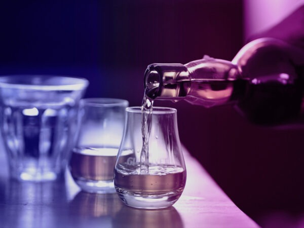 Eine Flasche Whisky wird in ein Glas gegossen, während zwei weitere Gläser auf einem Tisch stehen.