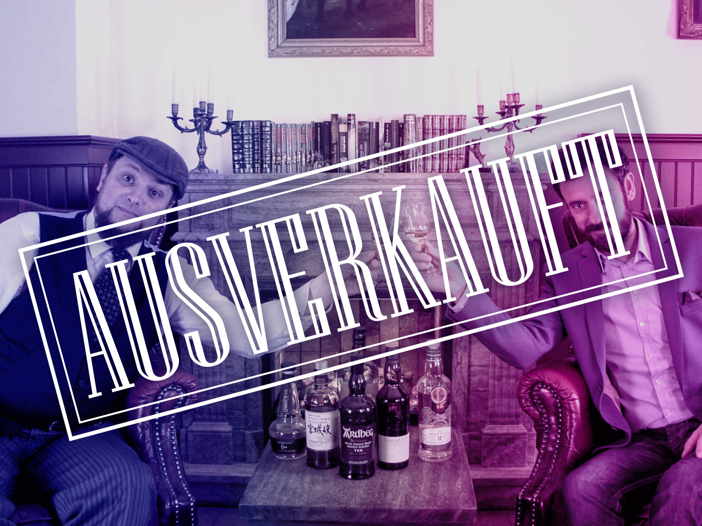 Zwei Männer in Anzügen sitzen auf einem Sofa mit Spirituosenflaschen im Hintergrund.