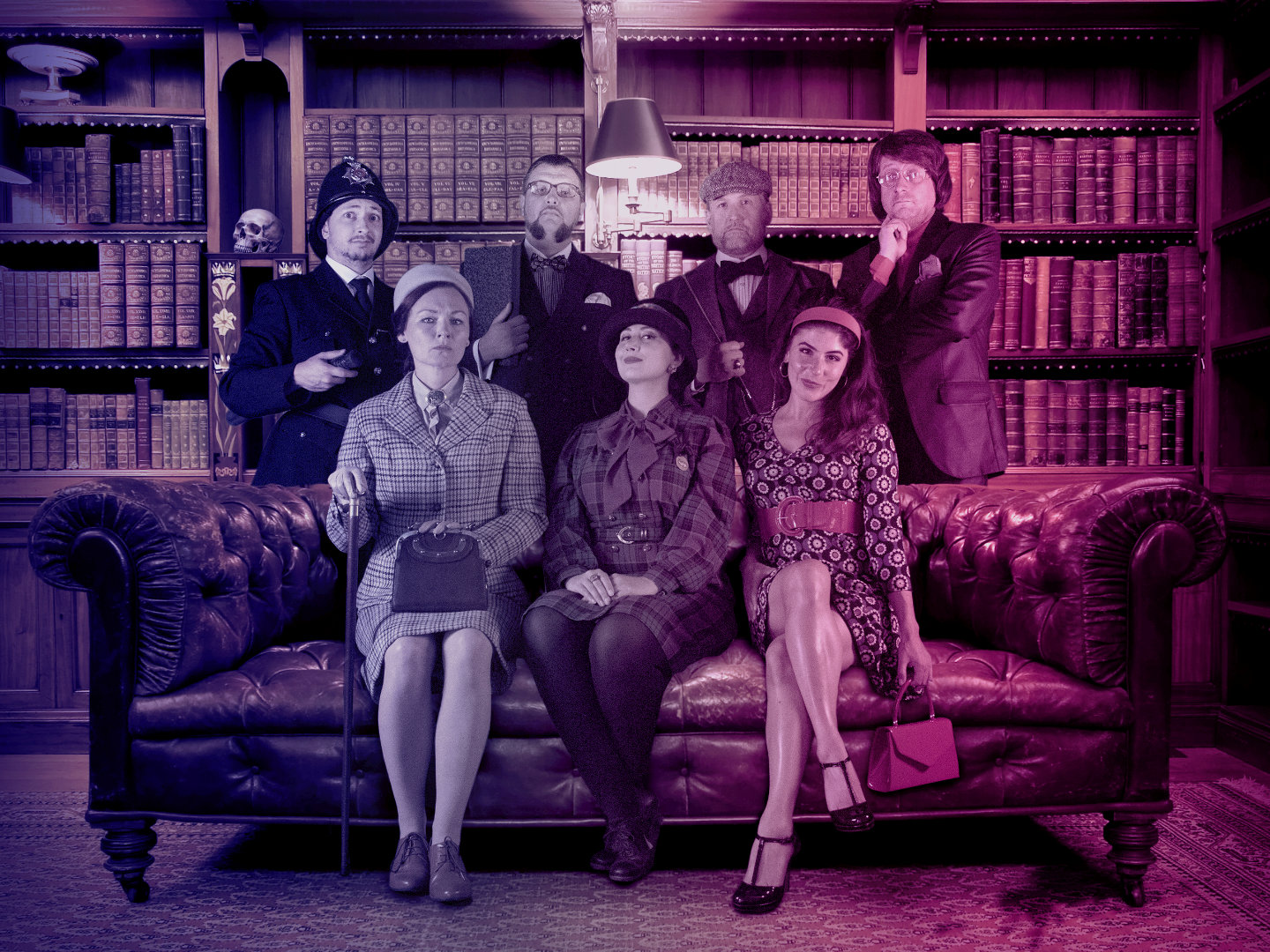 Sechs Personen in formeller Kleidung sitzen auf einem Ledersofa in einer Bibliothek.