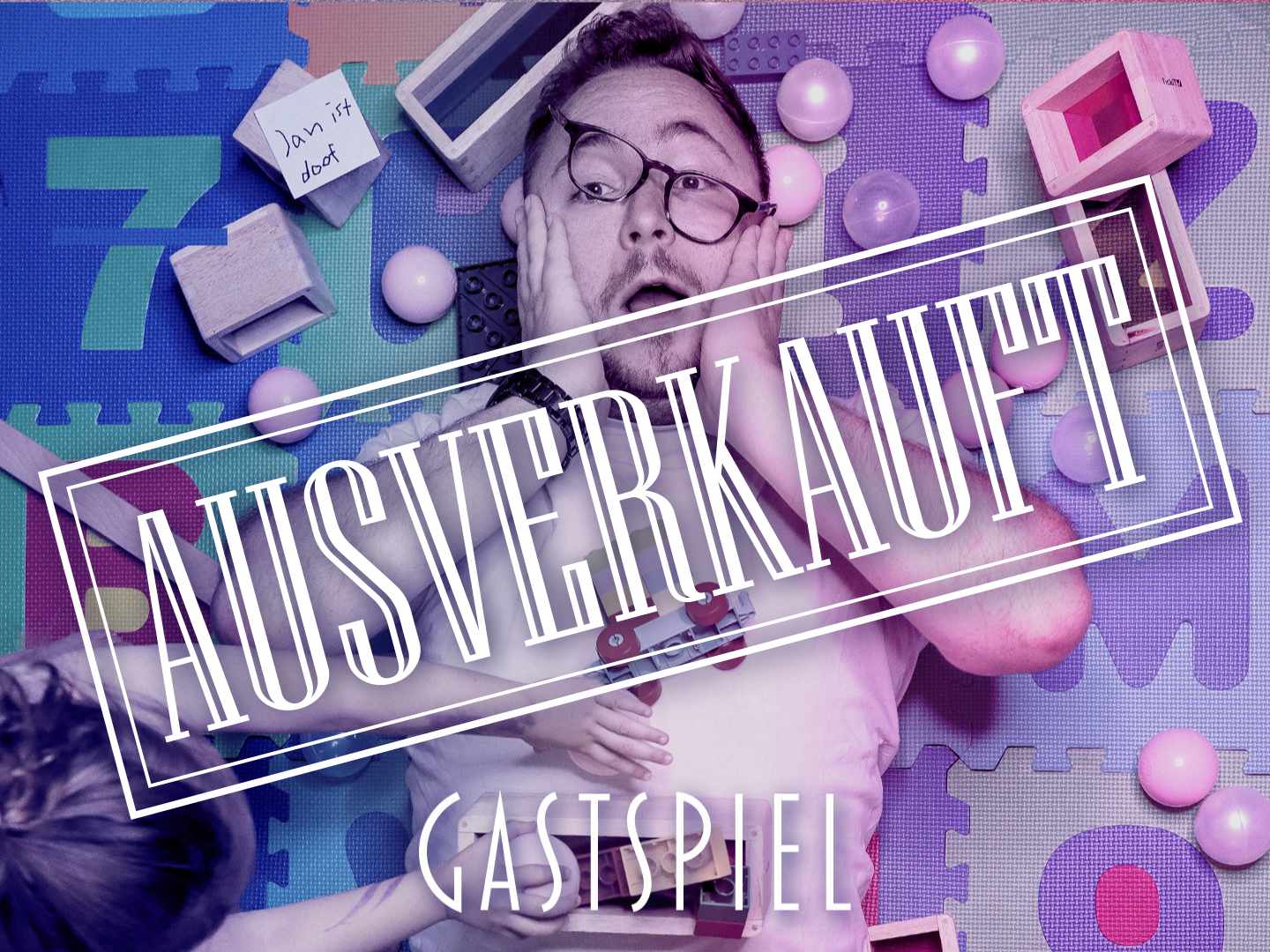 Ein Mann liegt auf dem Boden mit Spielzeug um ihn herum und hält sich das Gesicht mit beiden Händen.