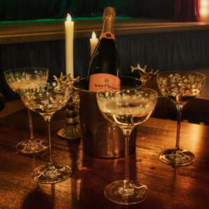 Eine Flasche Veuve Clicquot Champagner in einem Kühlbehälter mit drei Gläsern auf einem Holztisch.