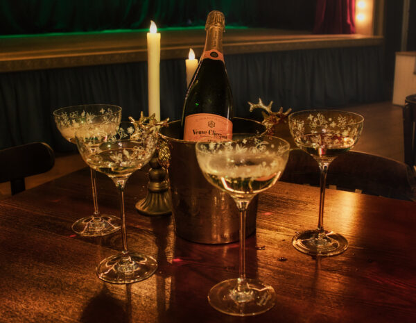 Eine Flasche Veuve Clicquot Champagner in einem Kühlbehälter mit drei Gläsern auf einem Holztisch.