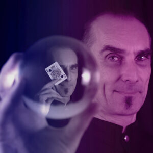 Magier hält eine Kristallkugel, in der sein Spiegelbild und eine Spielkarte sichtbar sind.